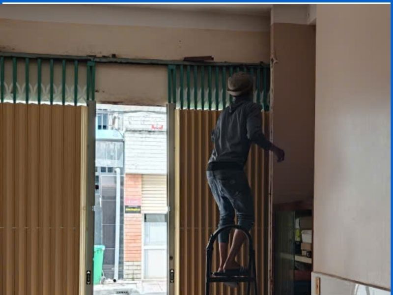 Thợ đứng thang xử lý nắn gài lá cửa kéo trên cao bị bung khỏi ngàm